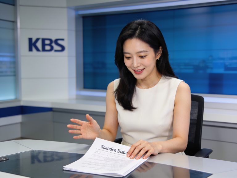 South Korean news anchor reviewing documents regarding KBS World entertainment scandals in a studio.